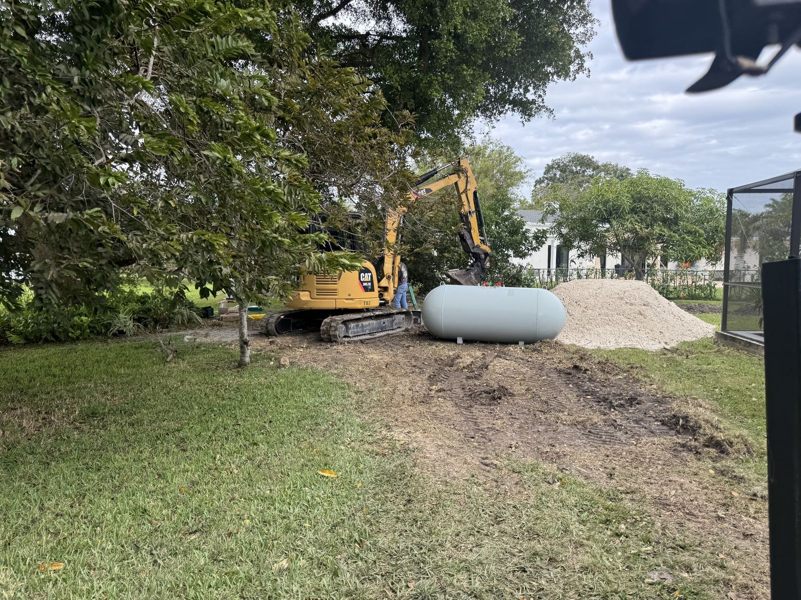 Excavator digging to set a buried propane tank beside a home